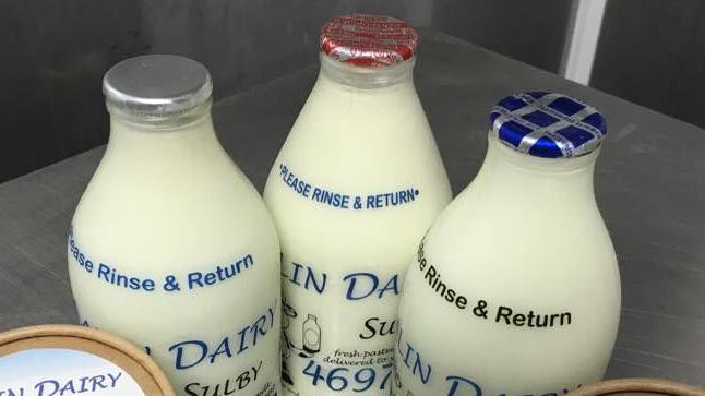 Three milk bottles full with white milk, with foil tops. One is silver, another is red, the third is blue.