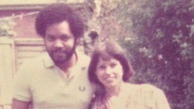 A grainy old printed out photograph of Thomas and Caroline. They are standing in a garden, wearing white, and smiling.