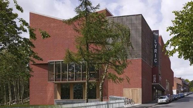 The Lyric Theatre in Belfast pictured from the outside.
A number of cars are parked out front and some trees can be seen as well.