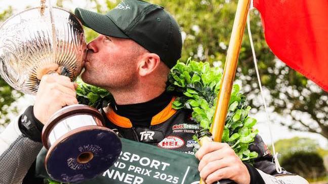 James Williams, who is wearing a green cap, kisses the Supersport trophy, which is a large silver cup.