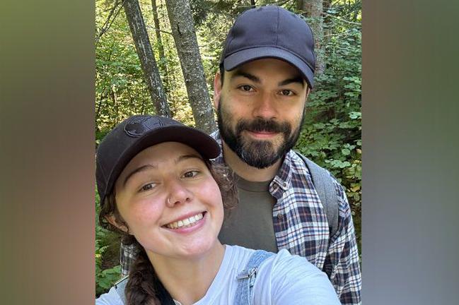 Mirelle Radley and her cousin Adam Radley are seen in a selfie. Both are wearing baseball caps. He has a dark brown beard and moustache and is wearing a checked shirt. She has her long hair in a plait and is wearing a white T-shirt and denim dungarees