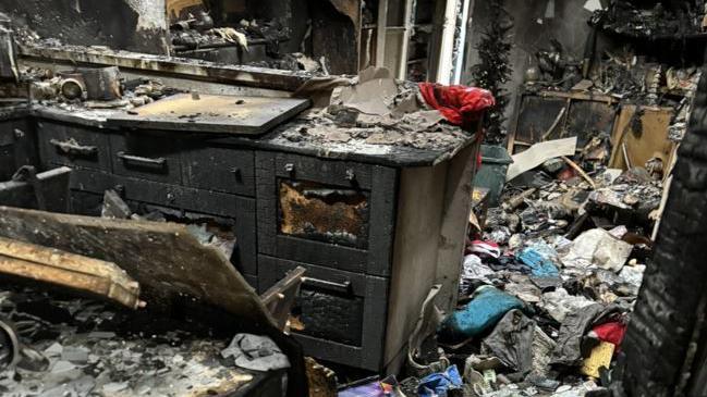 A view of the burned down living room of the bungalow. Heaps of charred items can bee seen scattered around. 