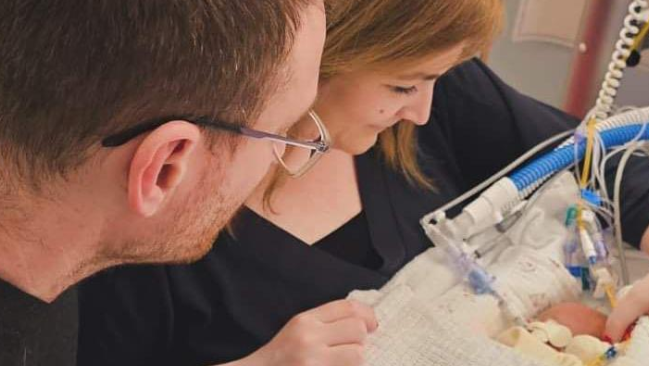 Mother and father leaning in to look at tiny baby in a hospital incubator unit