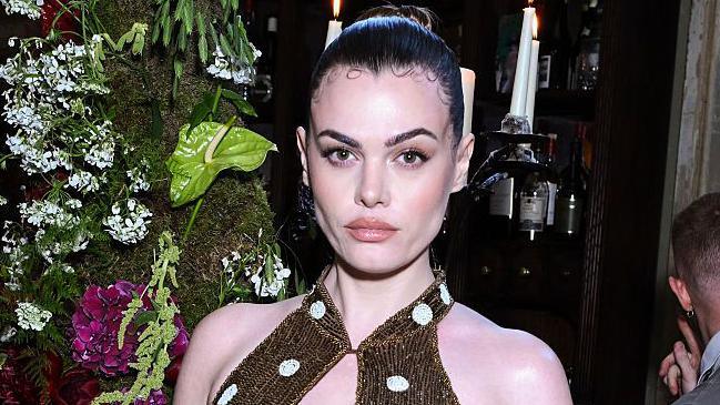 Model Charli Howard poses in a gold sparkly dress with white polka dots and her brown hair slicked back into a bun