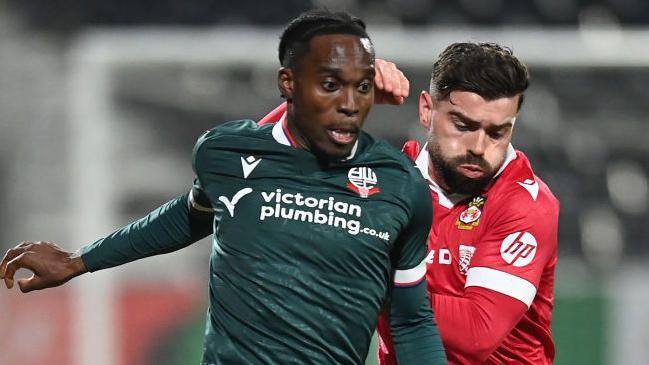 Bolton Wanderers' Jay Matete vies for possession with Wrexham's Elliot Lee during the Vertu Trophy Quarter Final match between Wrexham and Bolton Wanderers at Racecourse Ground