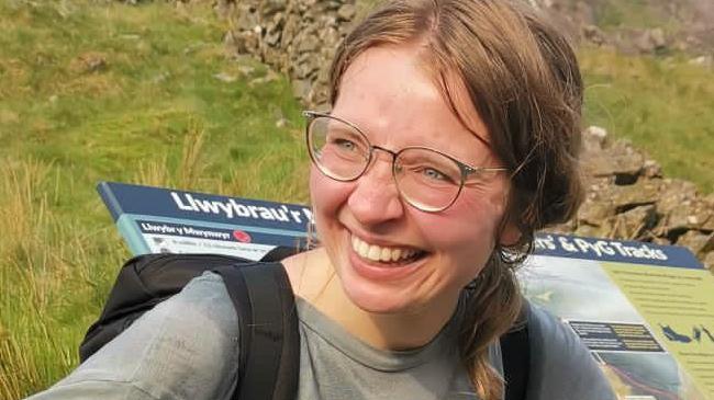 Karolina Pakenaite laughing in front of a sign for the path she followed up Yr Wyddfa