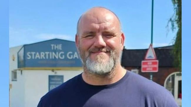 Councillor Peter Grogan is smiling at the camera. He has white beard and is wearing a navy blue t-shirt.