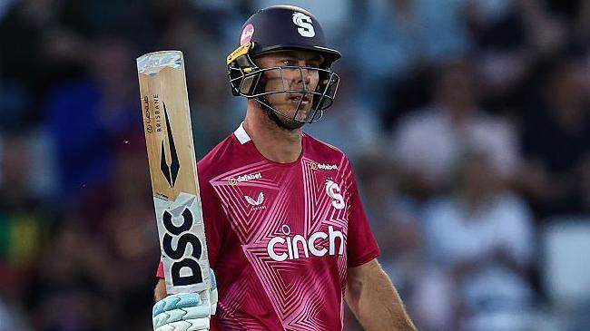 Chris Lynn, wearing a dark red shirt and navy helmet, raises his bat