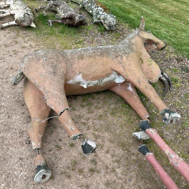 A concrete cow lying on its side with cracks in its legs
