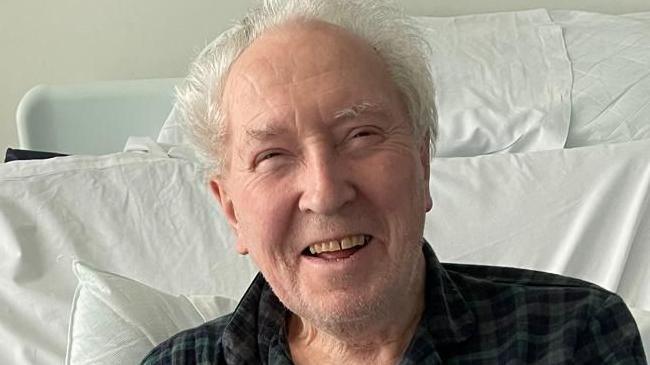 A smiling man with grey hair in a hospital bed