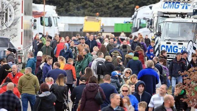 A crowd of people in between several large, white trucks
