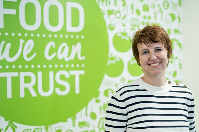 Rebecca Sudworth from the Food Standards Agency stood in a black and white stripey jumper in front of a green and white sign about food