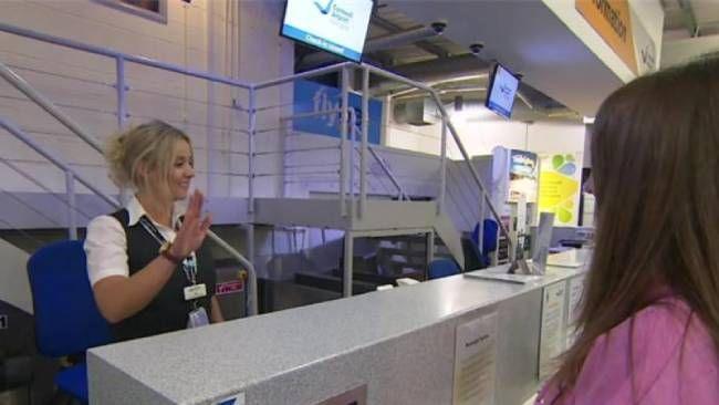 A woman working at an airport check in desk does Makaton signs while a passenger waits.