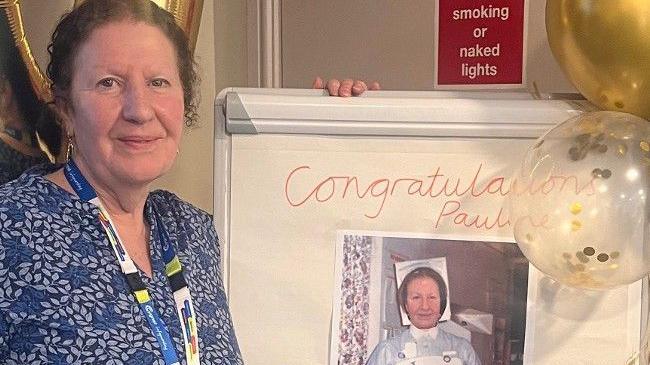 Pauline Rees celebrates next to poster of herself that says 'Congratulations Pauline'