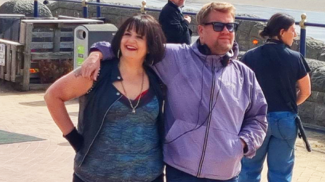 Gavin and Stacey writers and stars Ruth Jones - in character as Nessa - and James Corden with their arms around each other on Barry Island seafront, with filming crew and equipment nearby 