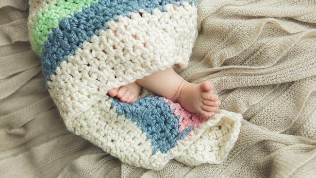 A generic image showing the close-up of the feet of a newborn baby wrapped in a knitted blanket.