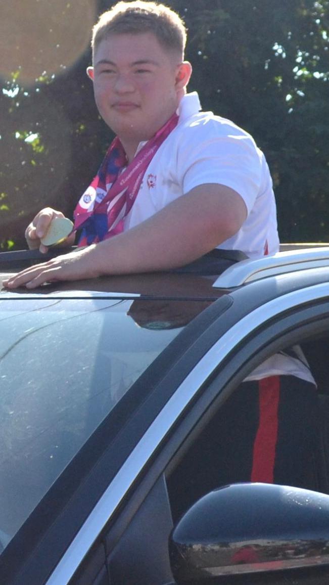 Bleddyn greets wellwishers through the sun roof of a vehicle, clutching his medals