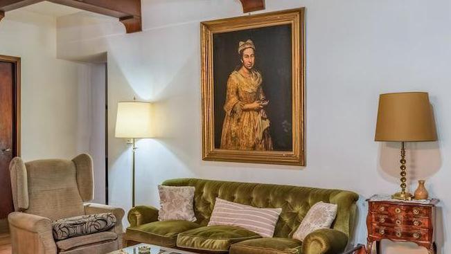 An interior shot showing a living room with a green sofa against a white wall, flanked by two lamps. A portrait hangs on the wall behind the sofa.