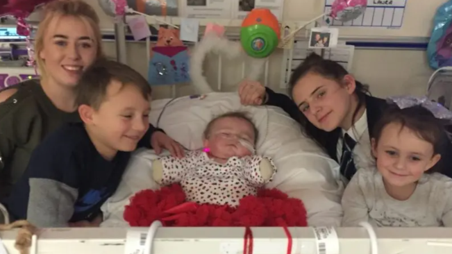 A baby in a hospital bed surrounded by family