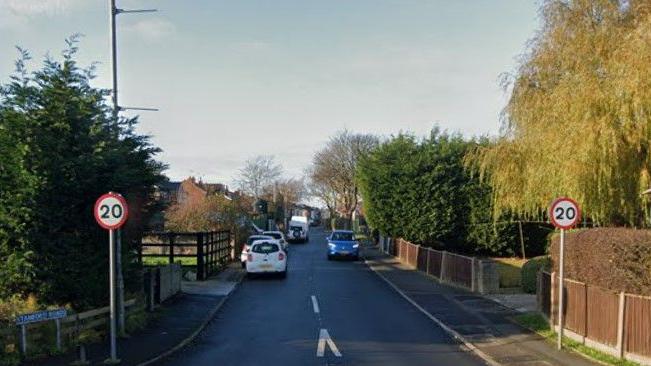 A Google street view image of Stamford Road, showing 20mph signs and houses and cars in the distance.