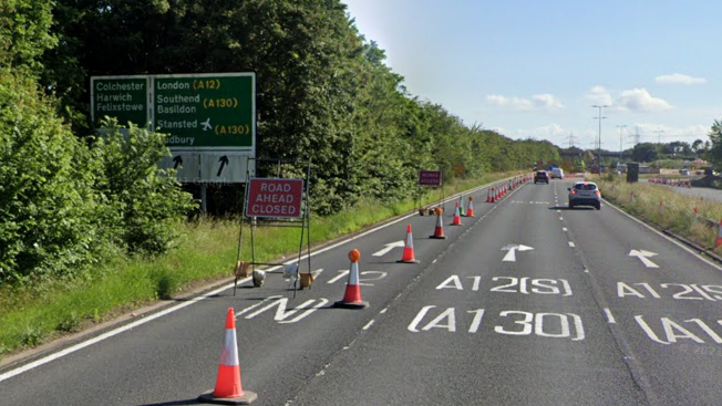 The A138, which has three lanes. The left-hand lane is closed and has cones blocking it. There is also a sign that says "road ahead closed" in the carriageway. There is a large road sign showing motorists the different directions they can go in, including to Colchester and London. There are cars in the distance using the middle and right lanes.