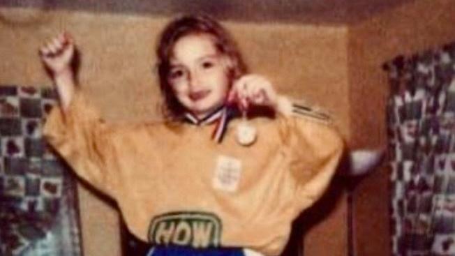 An image of a young girl in an orange and blue football kit showing her gold medal. 