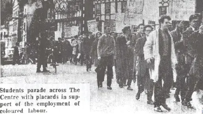 A black-and-white newspaper cutting shows students marching in Bristol in protest against a "colour bar" on the buses. They're holding placards and walking in a large group