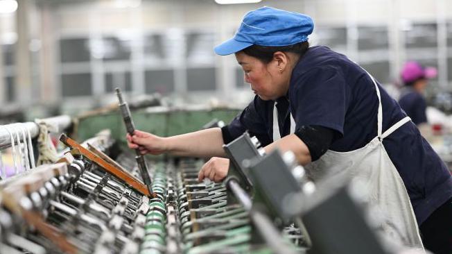 A female worker works on a spun silk production line at a Chinese factory. She is wearing a blue cap and a white apron over her navy blue uniform. 