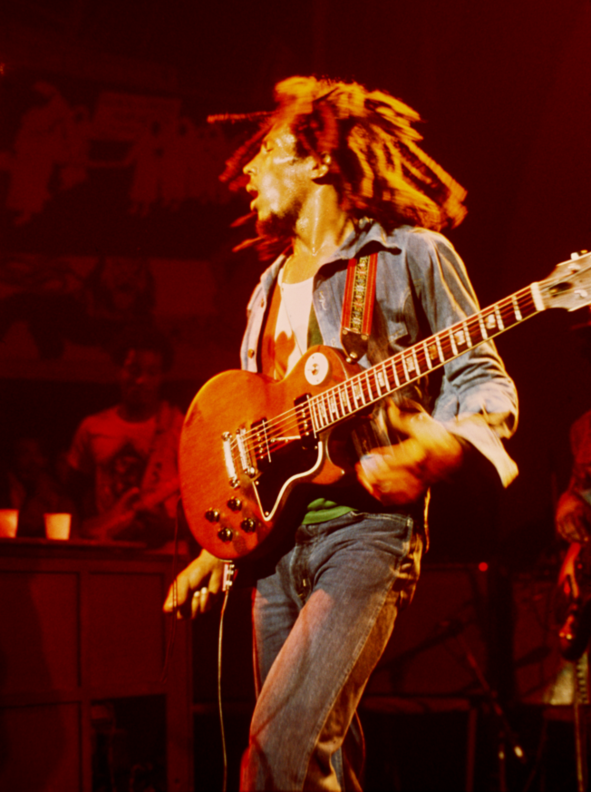 Colour photograph of Bob Marley with a guitar slung across his body in a live performance.