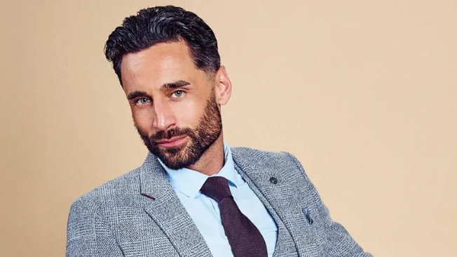 Luke Harden, dressed in a grey suit and purple tie in a modelling shot
