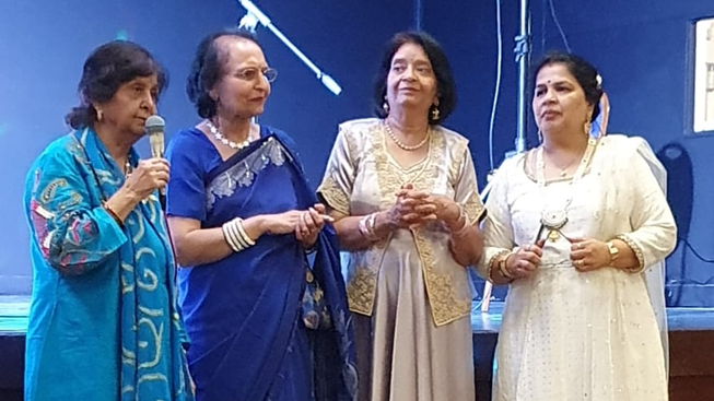 Four women speaking to a crowd. One is holding a microphone while the other three smile on.