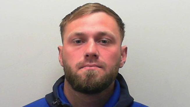 A custody picture of a man with short dark hair and a beard.