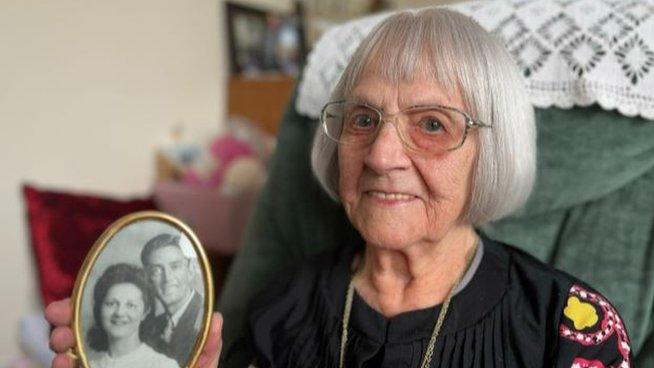 Grace Greenaway, holding a picture of herself and her husband Eirc