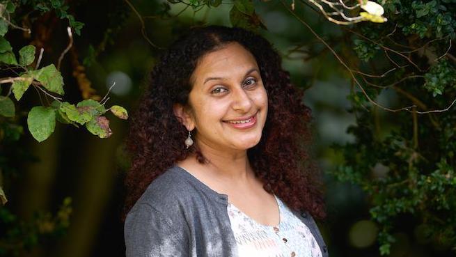 Krishna smiling at the camera, behind her are some trees.