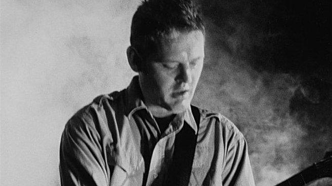 A black and white photo of Bruschini with his guitar