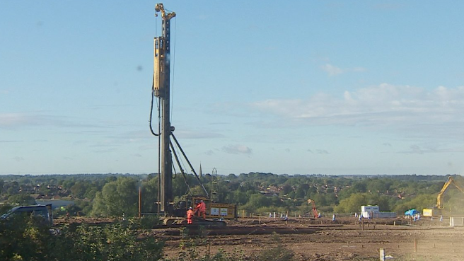 A large piling machine rising high into the sky over a building site  surrounded by trees