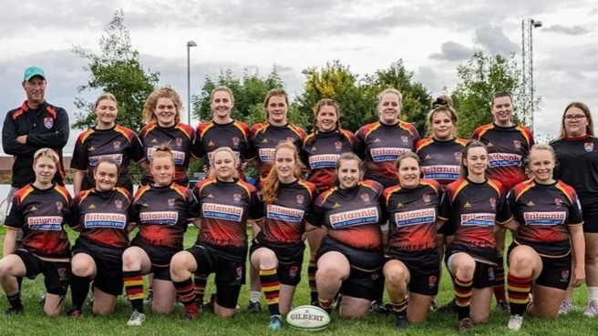 The Bridgwater and Albion Ladies team in their rugby kits.  They are standing on the pitch looking at the camera. The kits are black, yellow and red.