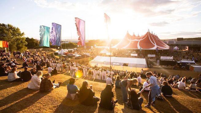Crowds looking down a hill at a big tent at a festival.