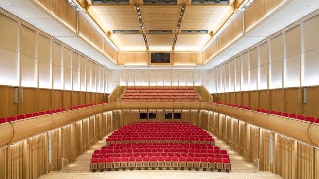 A large concert hall with rows of red seats on two levels.