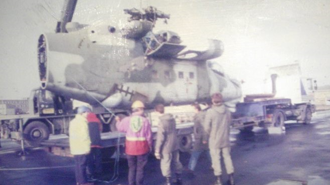 An old photograph of a helicopter being transported by an articulated lorry