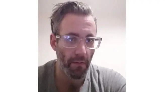 Image of Michael Wheeler wearing glasses. He is wearing a grey t-shirt and has a beard.