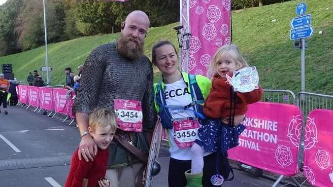 A man in a a Viking costume and a woman in running gear pose with their two children