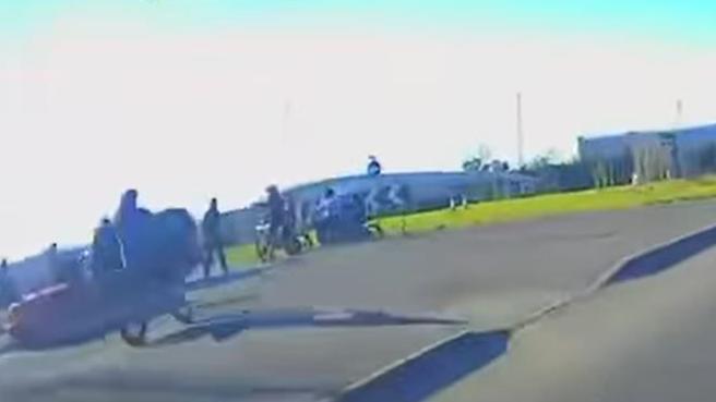 A still from dashcam footage showing a red car on a roundabout with a number of people on bikes around it