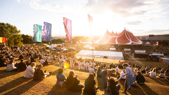 Crowds of people sitting on a grassy hill at the Rock N Roll Circus festival. 