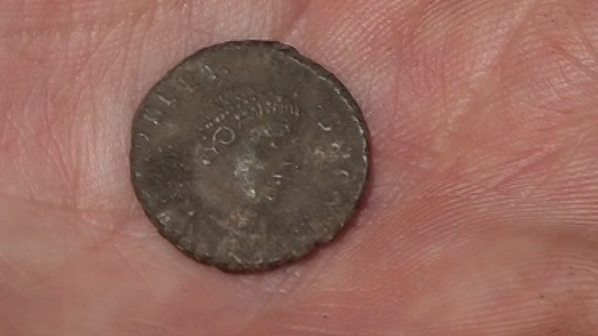 A portrait of the Emperor Valens on a gold coin held in the hand of an archaeologist at a dig in Guernsey 