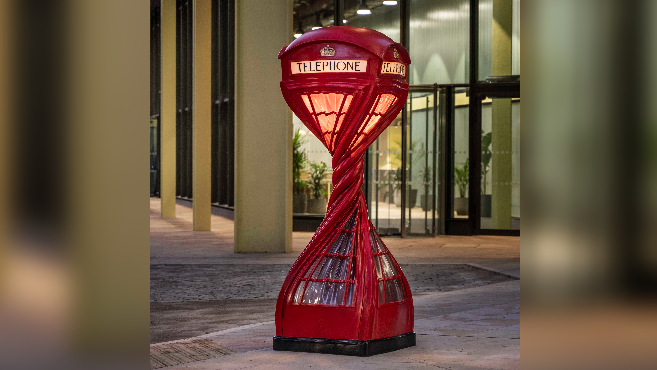 A red phone box twisted with a light on inside in front of an entrance to a building