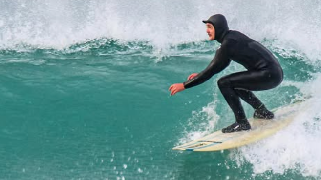 A surfer in a hooded wetsuit takes a right hand wave on a surfboard