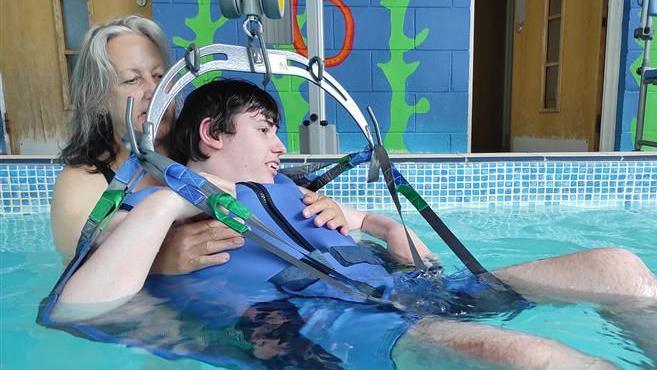 Ms Chaervey supports her son who is in a hoist within a hydrotherapy pool. 