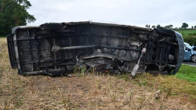 Uldis Stepins's van on its side on grass on the side of the road. The bottom of the van is facing the camera. 