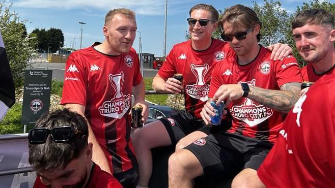 Five players smiling as they sit on the bus